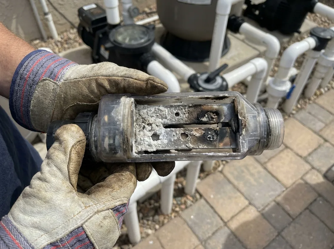 A pool technician holds a salt cell with electrode plates burnt and caked in scale, at the equipment pad